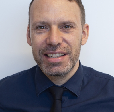 A picture of a man with short brown hair wearing a navy blue shirt and tie.