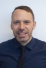 A picture of a man with short brown hair wearing a navy blue shirt and tie.